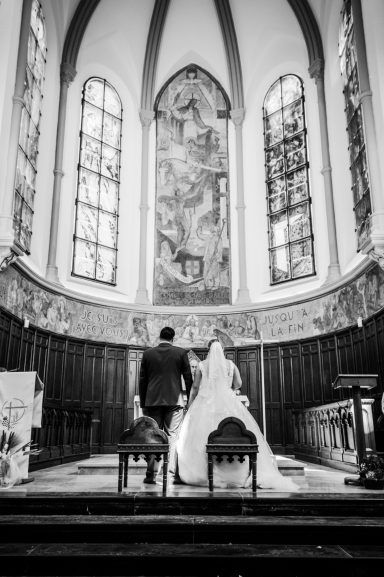 Un couple en arrière, face à l'autel dans une église, décorée de vitraux.