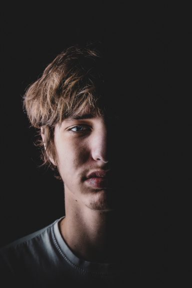 Portrait d'un jeune homme avec un éclairage contrasté, visage partiellement dans l'ombre.