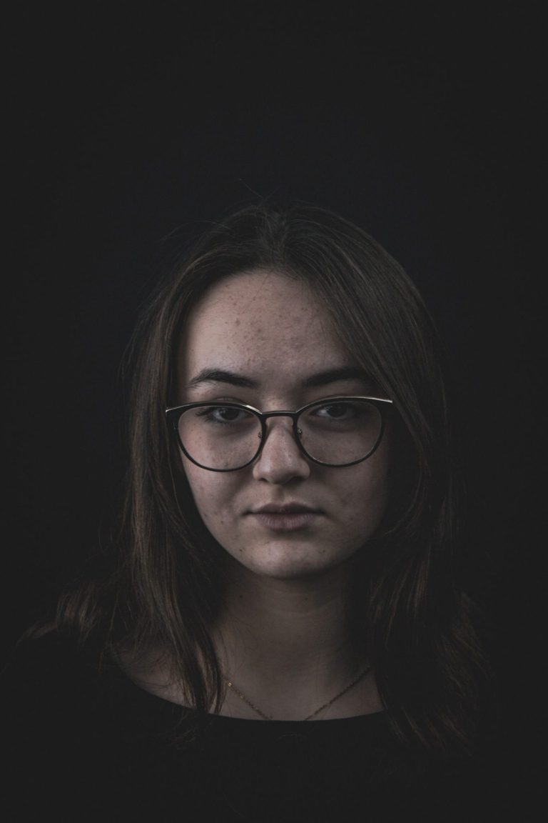 Portrait d'une jeune femme avec des lunettes, sur fond sombre.