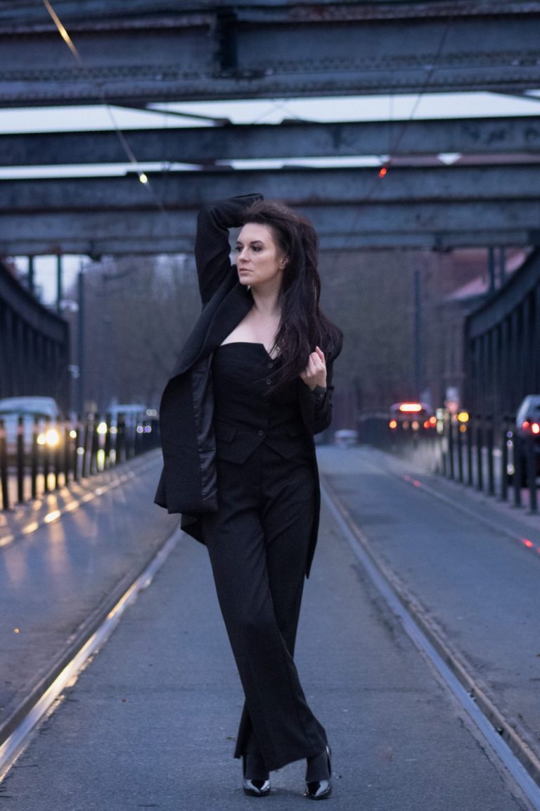 Femme en costume noir posant sur une voie ferrée sur un viaduc.